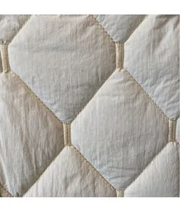 Detailed macro shot showing beige quilted rhombus pattern fabric texture with soft sheen