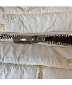 Macro view of silver metal zipper and quilted diamond pattern on white tote bag