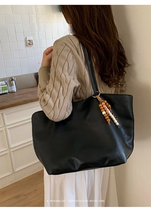 Detail of large black leather tote bag with stylish wooden bead tassel and long straps