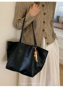 Detail of minimalist black tote bag featuring delicate shoulder straps and wooden beads