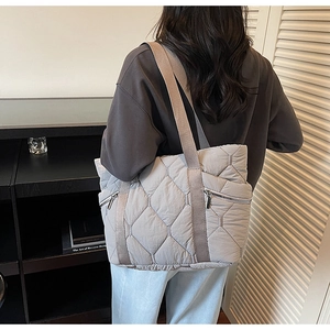 Macro detail of quilted puffer tote bag featuring silver side zipper and soft fabric texture