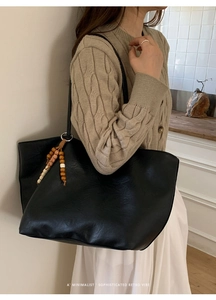 Close-up of large black leather tote bag featuring a decorative beaded charm on the side