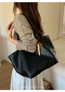Detail of large black tote bag with wooden bead charm on a shoulder worn by a model