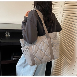 Close-up of grey quilted tote bag featuring silver side zippers and padded straps