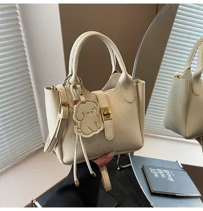 Detail of cream lychee grain leather bucket bag with logo and cute dog charm accent