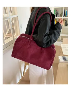 Detalle del bolso tote de ante burdeos con cremallera plateada sobre chaqueta de cuero
