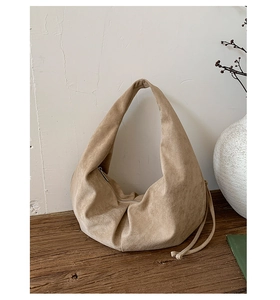 Detailed view of beige suede hobo bag with drawstring and zipper on wooden desk