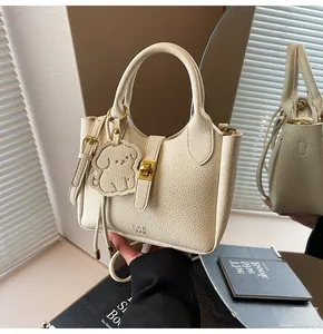 Detail of cream lychee texture leather bucket bag with gold turn-lock and dog charm