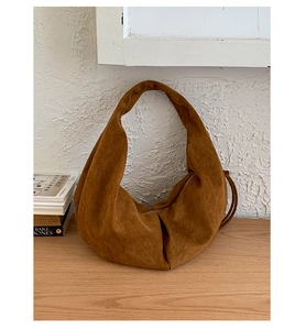 Detail of a brown suede hobo bag with zip closure on a wooden table in soft light