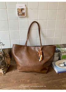 Close-up of vintage brown tote bag with leather texture and wooden bead tassel detail