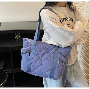 Detail of blue quilted tote bag with silver zippers and wide fabric straps for women