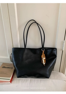 Detail of black leather tote bag with vintage texture and colorful wooden bead pendant