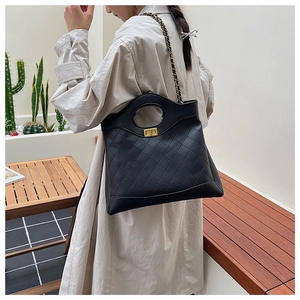 Close-up of black quilted leather bag with gold rectangular turn-lock and chain strap