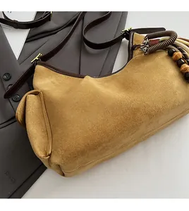 Détail du sac hobo en daim camel avec perles en bois sur un blazer gris foncé