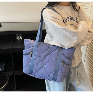 Close-up of quilted blue tote bag featuring diamond stitching and dual silver zipper pockets