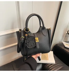 Close-up of black pebbled leather bucket bag featuring gold twist lock and bear charm