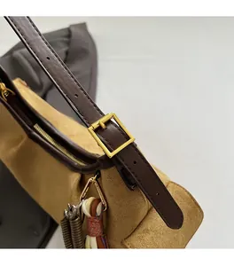 Détail de la bandoulière en cuir et des boucles dorées sur un sac en daim marron vintage
