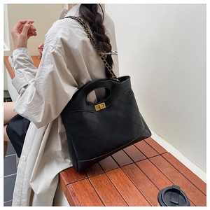 Detail of black quilted leather tote bag with gold chain strap and hollow handle on a bench