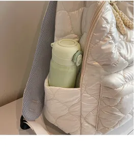 Detail of a beige quilted backpack side pocket holding a green water bottle