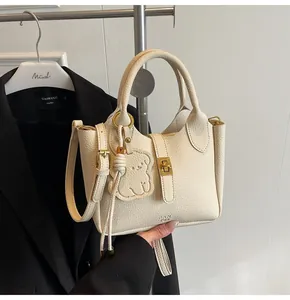 Detail of cream lychee texture leather bucket bag with gold lock and bear charm