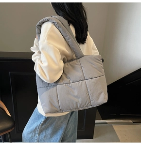 Borsa tote grigia trapuntata con ampia tracolla indossata da una modella, stile minimal