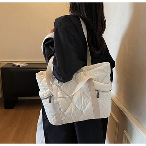 Detail of white quilted tote bag featuring silver side zippers and woven shoulder strap