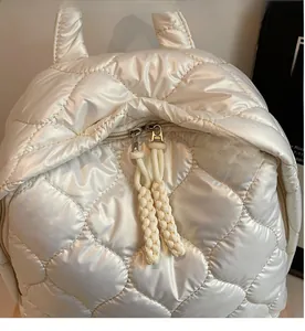 Detail of smooth metal zipper with woven knot puller on cream quilted backpack