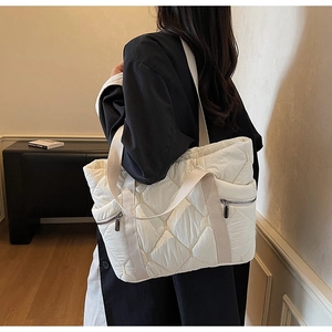 Detail of white quilted tote bag featuring metal side zipper and wide shoulder strap