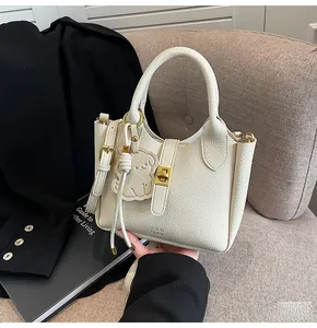 Detail of lychee textured leather bucket bag with gold lock and cute charm on sofa