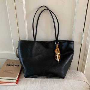 Detailed view of black tote bag featuring double handles and ethnic wooden bead tassel charm