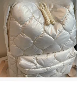 Macro view of quilted white puffer backpack with braided rope zipper and glossy texture