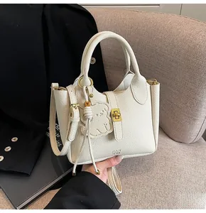 Close-up of beige lychee texture leather bucket bag with gold hardware and bear charm