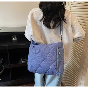 Detail of blue quilted nylon crossbody bag showing side zipper pocket and texture
