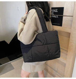 Vista a spalla di una borsa tote nera trapuntata con ampia capacità e manici imbottiti