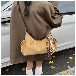 Détail du sac bandoulière en daim jaune avec finitions en cuir brun et pompon ethnique