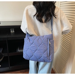 Detail view of blue quilted tote bag showing the side zipper and puffer texture
