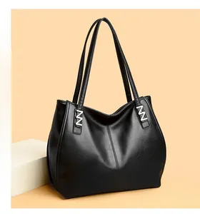 Close-up of black lychee grain tote bag with silver letter hardware on orange background