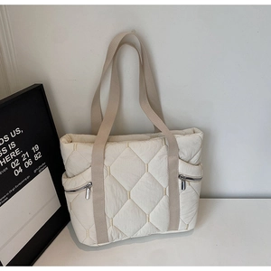 Detail of quilted diamond pattern and metallic zipper pockets on cream tote bag