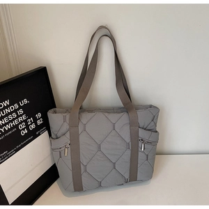 Macro detail of grey quilted tote bag with brown straps and side zipper pockets