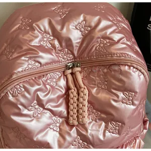 Detailed close-up of pink metallic quilted fabric with embossed bow and smooth dual zippers