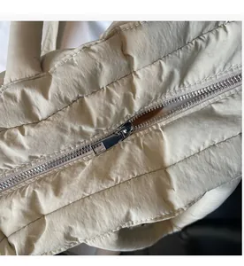 Detail showing smooth silver metal zipper on cream quilted puffer tote bag fabric