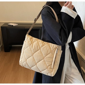 Detail of cream quilted tote bag with brown leather strap and decorative side zipper