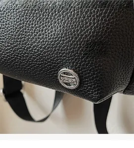 Detailed macro view of black lychee grain texture and round silver metal ornament on bag