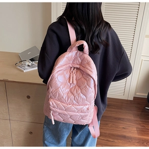 Detail of pink heart-quilted nylon backpack showing glossy texture and zippered pockets