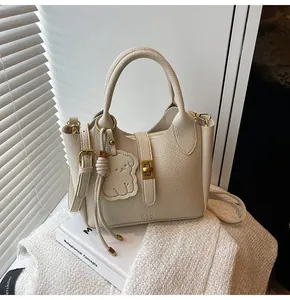 Detail view of beige lychee leather bucket bag with gold hardware and bear charm accessory