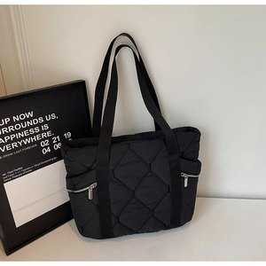 Macro detail of black quilted tote bag showing side zipper and rhombus stitched texture