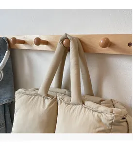 Detail of beige quilted tote bag hanging on wooden hook with soft padded texture