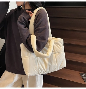 Dettaglio della borsa shopper trapuntata beige con manici imbottiti su una scala in legno