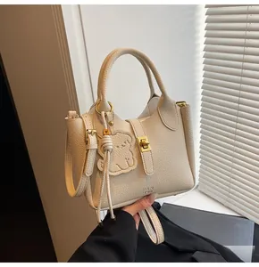 Detail of cream lychee texture leather bucket bag with gold clasp and bear charm