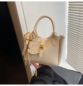 Detail of beige lychee leather bucket bag with gold twist lock and dog charm